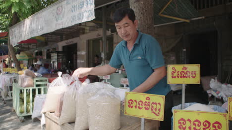 Merchant-adjusting-his-bag-with-different-varieties-on-a-outdoor-rice-market-in-Phnom-Penh