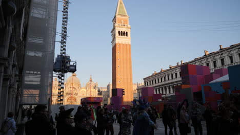 Golden-Hour-on-St-Mark's-Square-During-Carnival-Time,-Tilting-View-of-St-Mark's-Campanile-Belltower,-People-Gathering-in-Carnival-Costumes