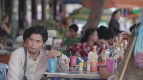 Junge-Kambodschaner-Nippen-An-Einem-Großen-Restauranttisch-Im-Freien-In-Phnom-Penh-An-Einer-Tasse