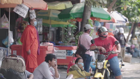 Street-market-scene-with-monk-wearing-face-mask-in-Phnom-Penh-Cambodia