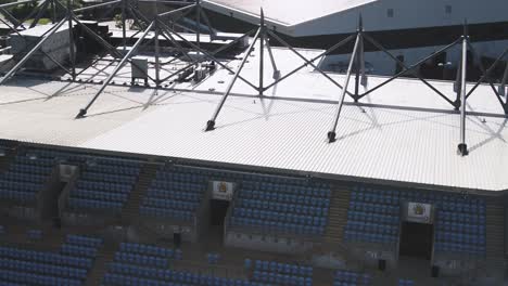 Aerial-dropping-and-tilting-up-to-reveal-modern-stadium-seating-and-roofing-at-Sandy-Park,-Exeter,-Devon