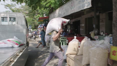 Man-unloading-heavy-bag-of-rice-from-a-truck-at-outdoor-rice-market-in-Phnom-Penh