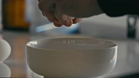 Hands-opening-raw-egg-into-a-white-bowl-to-make-breakfast