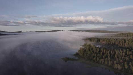 Fog-covered-forest-lake-below-morning-blue-sky-Scandinavian-landscape-DRONE