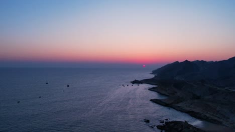 Sunset-over-ocean-with-mountain-silhouettes,-aerial-view