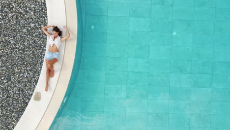 Top-down-aerial-view-of-a-young-woman-posing-beside-a-pool