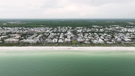 Slide-to-right-motion-full-view-of-Rosemary-beach-town-with-coastline-upfront-and-horizon-cloudy-sky-in-the-back