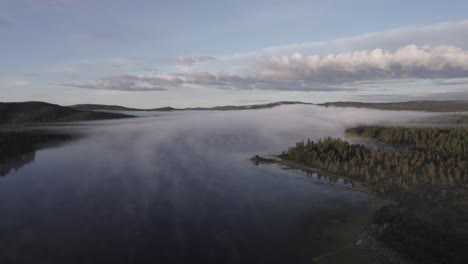 Morning-fog-over-tranquil-lake-reflects-forest-Norwegian-landscape-DRONE