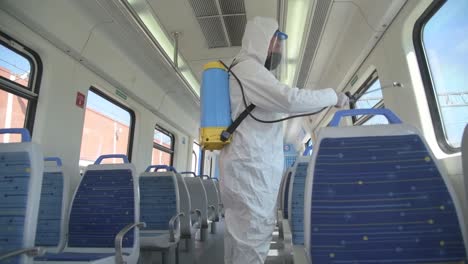 Worker-sprays-disinfectant-solution-across-public-transit-tram-rail-seats-wearing-white-suit