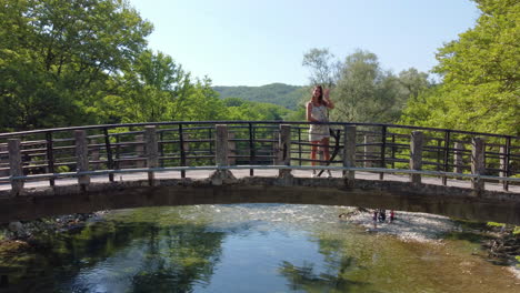 Eine-Frau-Posiert-Auf-Der-Aristi-Brücke-Und-Genießt-Die-Malerische-Aussicht-Auf-Die-Natürliche-Schönheit-Rund-Um-Den-Berühmten-Fluss-Voidomatis,-Der-Durch-Den-Vikos-Nationalpark-In-Epirus,-Griechenland,-Europa-Fließt