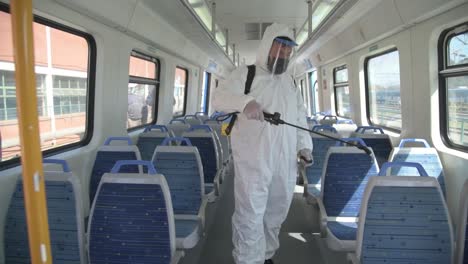 Man-in-hazmat-protective-one-piece-coverall-suit-sprays-disinfectant-on-public-transit-seating