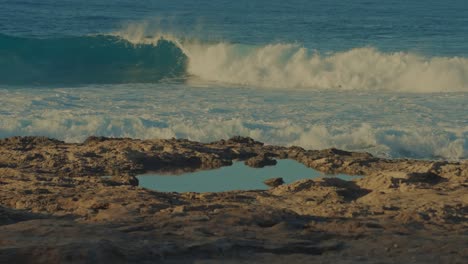 a-wave-crests-to-a-perfect-roll-in-the-turquoise-Pacific-waters-on-the-island-beach-in-Oahu-Hawaii-with-a-tide-pool-in-the-foreground