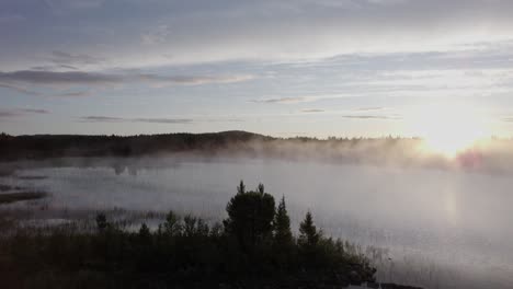 Eerie-morning-sunrise-mist-over-tranquil-forest-lake-Norway-landscape-DRONE