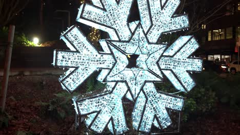 Rising-reveal-large-white-snowflake-christmas-decoration-sat-on-a-verge-in-a-local-city-park-in-the-Canadian-city-of-Vancouver-at-night-causing-a-festive-glow