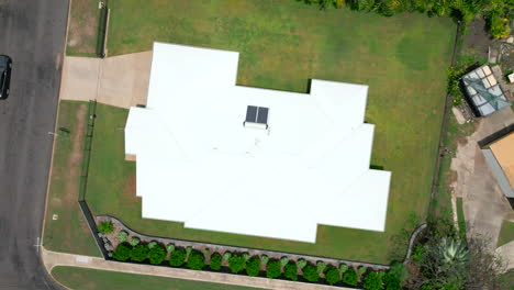 Weißes-Wellblechdach-Eines-Hauses-Mit-üppigen-Grünen-Rasenflächen,-Luftdrohnenaufnahme