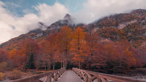 Vorderansicht-Der-Brücke-über-Den-Fluss-Am-Eingang-Des-Ordesa-Nationalparks-Im-Herbst-Mit-Wunderschönen-Baumfarben,-Schneebedeckten-Gipfeln-Und-Wanderern