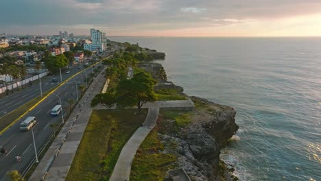 Aerial-flight-along-coastline-of-Santo-Domingo-with-traffic-at-MARITIMO-PROMENADE-during-sunset-time---Establishing-drone-shot