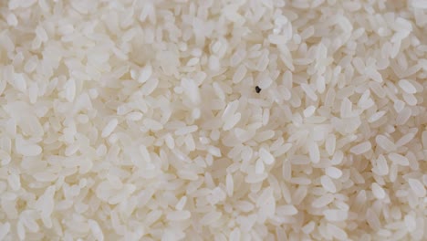 Saubere-Körner-Aus-Poliertem-Weißem-Reis-Fallen-In-Nahaufnahme-Mit-Schwarzen-Kieselsteinen