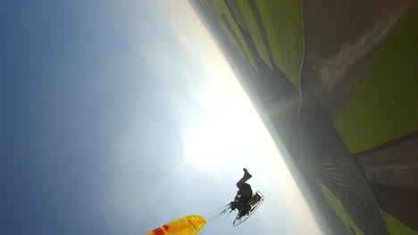 Vertical-format:-Aerial-orbits-yellow-paramotor-glider-in-blue-sky