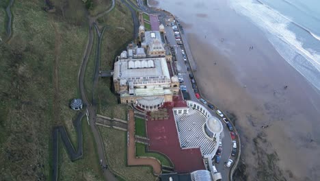 Aerial-side-view-shot-of-top-of-vacant-Scarborough-Spa-with-beautiful-cityscape-at-background-and-a-beach-beside-it-in-North-Yorkshire,-England