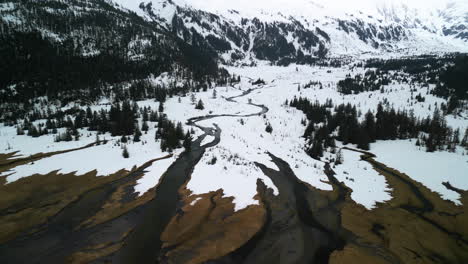 Aerial-view-following-a-winding-river-in-middle-of-snowy-mountains-in-cloudy-Alaska