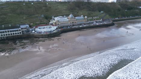 Cinematic-shot-of-continuous-tides-at-the-beach-with-some-people-enjoying-beside-Scarborough-Spa-in-North-Yorkshire,-England