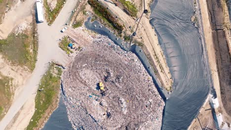 Wide-shot-of-a-drone-over-a-mountain-of-garbage,-a-truck-is-pushing-the-garbage,-there-are-lots-of-birds-flying-over-the-trucks