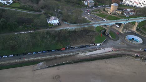 Parallax-aerial-shot-of-a-metal-foot-over-bridge-over-a-busy-road-with-cars-parked-at-a-side-of-it-in-Scarborough-bay,-England