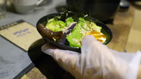 Bowl-full-of-nutritious-asian-vegetable-and-egg-moved-by-hand-on-kitchen-table,-filmed-as-closeup-slow-motion-style-shot