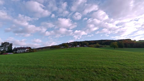 Schwenkaufnahme-Von-Holzhäusern-Entlang-Einer-Grünen-Wiese-Entlang-Eines-Hügelhangs-Inmitten-Ländlicher-Landschaft