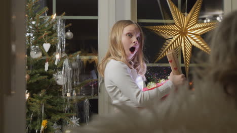 Young-girl-opening-a-magical-sparkly-Christmas-gift-in-awe,-warm-indoor-holiday-setting