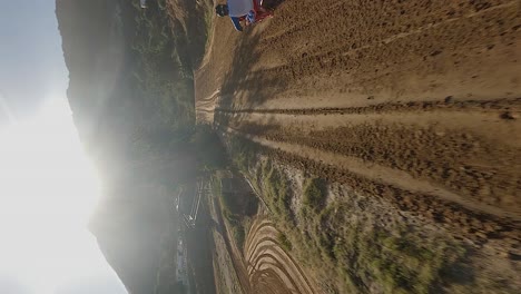 Vertical-format:-Aerial-follows-moto-racer-into-the-sun-on-dirt-track