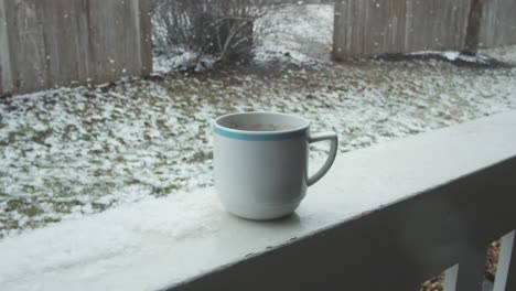 Close-up-on-coffee-mug-on-balcony-view,-snow-falling-on-background,-gimbal-shot,-camera-pulling-down,-day