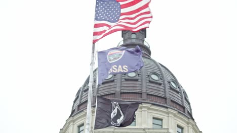 Edificio-Del-Capitolio-Del-Estado-De-Kansas-Con-Banderas-Ondeando-En-Topeka,-Kansas-Con-Primer-Plano-De-Banderas-Video-Estable