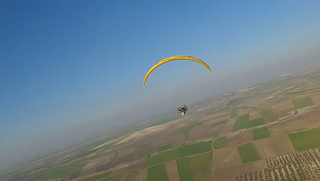 Aerial-follows-motor-paraglider-flying-high-over-farmland-crops