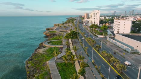 Drone-establishing-flight-along-coastal-road-of-Malecon-District-and-traffic-at-golden-hour---Beautiful-Landscape-in-Santo-Domino-Town,-Dominican-Republic