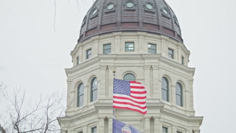 Kansas-state-capitol-building-with-flags-waving-in-Topeka,-Kansas-with-close-up-video-tilting-down
