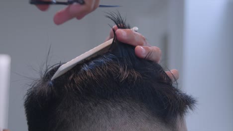 Smooth-black-hair-on-top-of-head-being-measured-by-hand-and-comb-then-cut-by-scissors,-filmed-as-closeup-shot-in-handheld-style-on-right-side-of-head