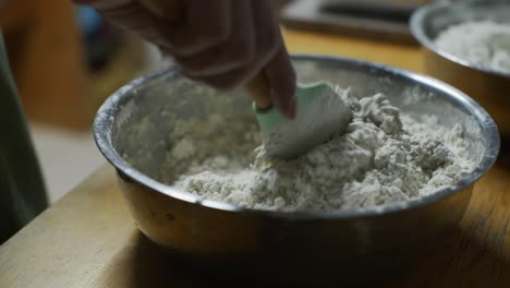 Soft-and-fluffy-flour-dough-mix-spoon-mixed-by-hand-in-steel-bowl,-filmed-as-closeup-shot-in-handheld-slow-motion-style