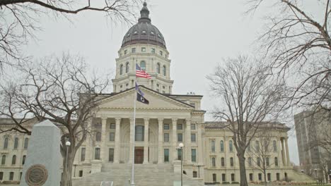 Kansas-state-capitol-building-with-flags-waving-in-Topeka,-Kansas-with-wide-shot-video-in-slow-motion.
