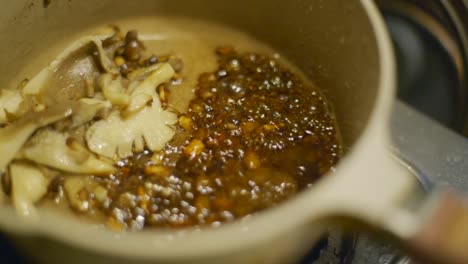 Mushroom-and-dark-soy-bean-sauce-sizzling-and-bubbling-in-gray-pot-over-gas-stove,-filmed-as-closeup-slow-motion-shot-in-handheld-style