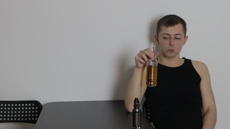 Depressed-young-Caucasian-man-sitting-alone-inside-a-room-vaping-and-drinking-beer