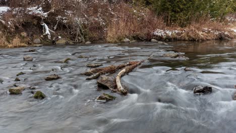 Timelapse-of-river-water-rushing-over-rocks-and-branches-in-winter