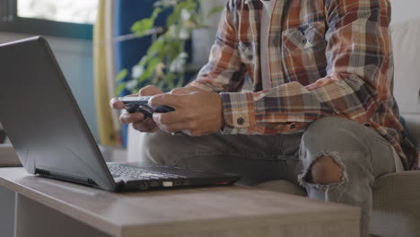 Young-adult-freelancer-working-from-home-in-his-living-room-using-laptop,-is-distracting-by-playing-mobile-games-and-watching-funny-videos-content-in-social-networks