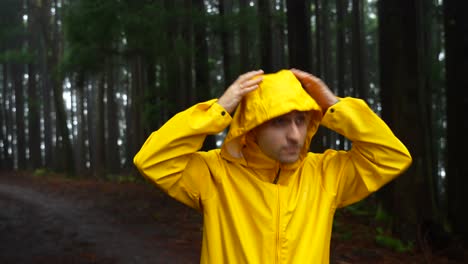 Young-man-zipping-bright-yellow-raincoat-in-dark-rainy-forest,-looking-around