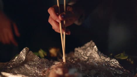 Chopsticks-used-to-remove-flesh-off-freshly-barbecue-baked-fish-on-foil,-filmed-as-closeup-shot-in-slow-motion-style