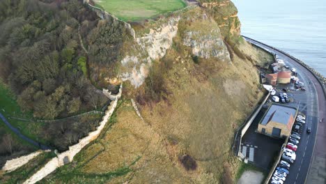 Aerial-parallax-shot-of-a-road-near-hill-cliff-beside-a-ocean-during-daytime-in-Scarborough,-England