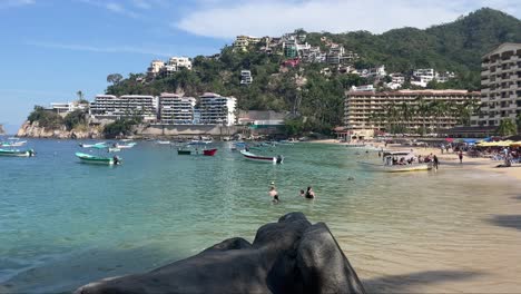 Static-establishing-view-of-Mismaloya-Mexico-beach-with-tourists-playing-in-water-by-anchored-boats