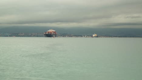 Container-vessel-moored-near-Gibraltar-harbor,-time-lapse-view-with-stormy-clouds