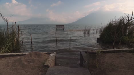 Peaks-of-the-Three-Giants-volcanos-in-Guatemala-hidden-in-clouds-with-calm-water-of-Lake-Atitlan-in-foreground